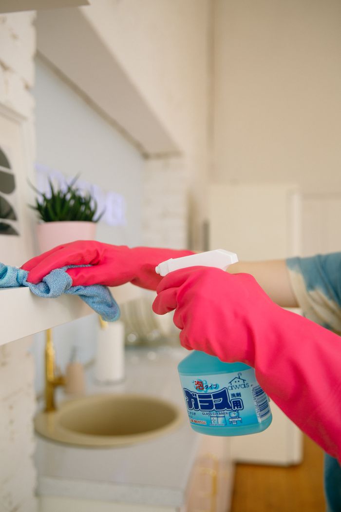 hero-img-01 A person using a spray bottle and cloth to clean a kitchen shelf, helping maintain hygiene and cleanliness.